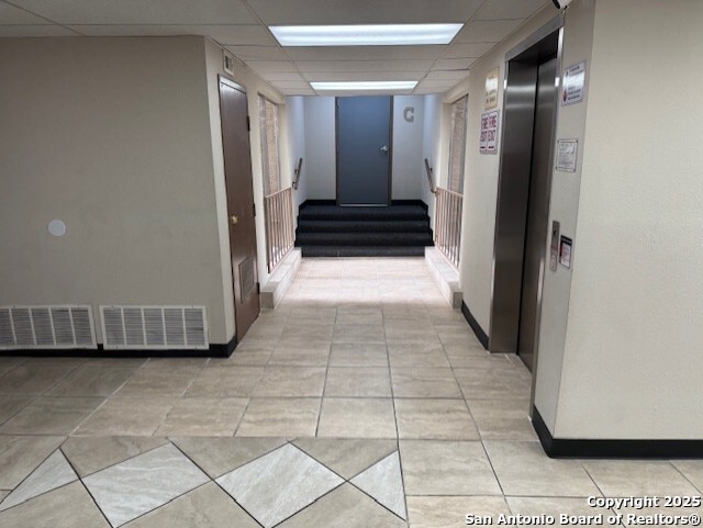 hallway featuring a paneled ceiling, elevator, visible vents, and light tile patterned floors