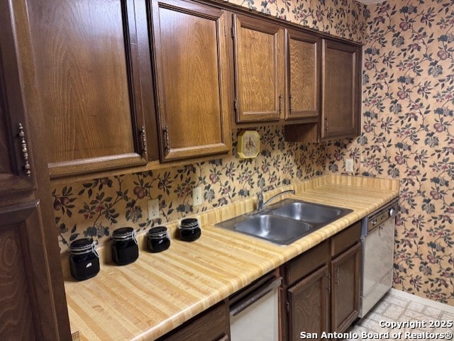 kitchen featuring light countertops, dishwasher, a sink, and wallpapered walls