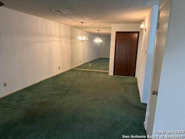 empty room featuring a textured ceiling, dark carpet, visible vents, and a notable chandelier