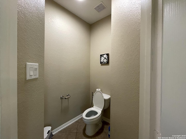 bathroom featuring visible vents, a textured wall, toilet, baseboards, and tile patterned floors