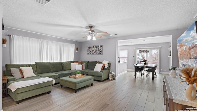 living area featuring light wood-type flooring, ceiling fan, visible vents, and a textured ceiling