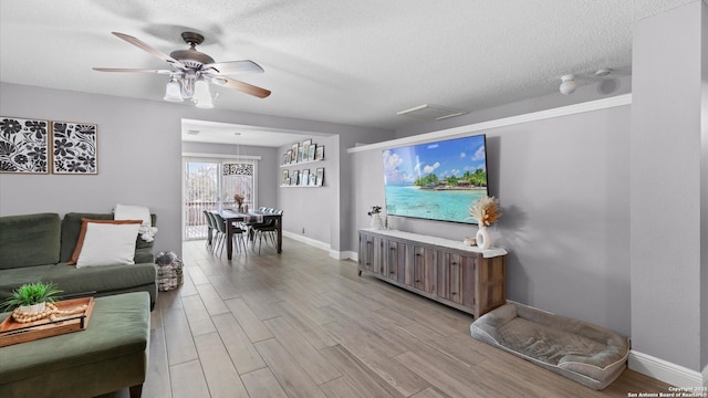 living area with a textured ceiling, visible vents, baseboards, a ceiling fan, and light wood-style floors