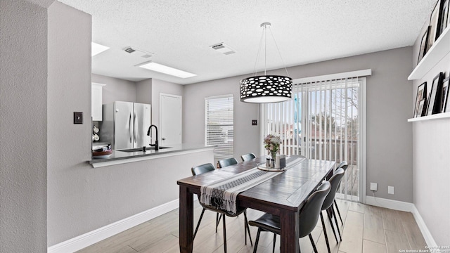 dining room with baseboards, visible vents, light wood finished floors, and a textured ceiling