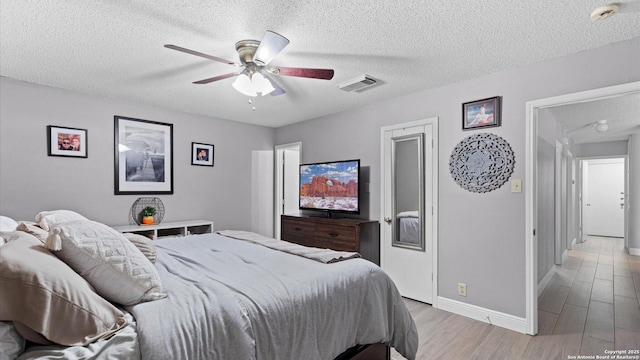 bedroom featuring baseboards, visible vents, a ceiling fan, light wood-style flooring, and a textured ceiling