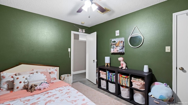 bedroom featuring ceiling fan, a textured wall, a textured ceiling, and wood finished floors