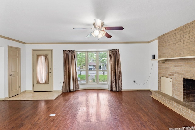 unfurnished living room featuring a brick fireplace, crown molding, baseboards, and wood finished floors