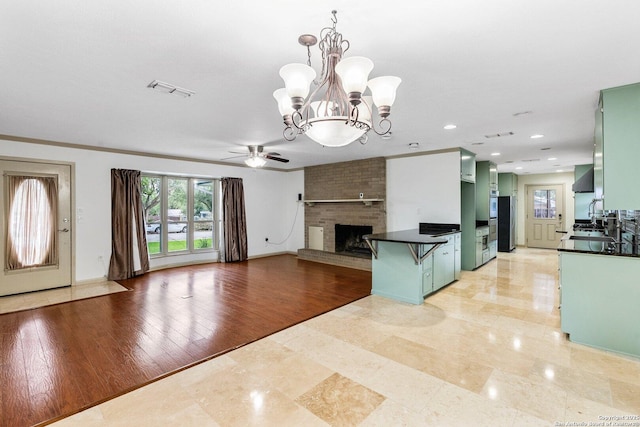 kitchen with dark countertops, wall chimney exhaust hood, open floor plan, a kitchen bar, and green cabinets