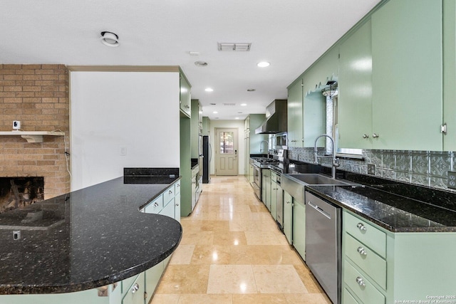 kitchen with a peninsula, wall chimney exhaust hood, appliances with stainless steel finishes, and green cabinetry