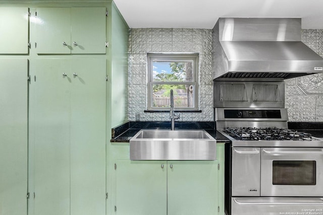 kitchen with tasteful backsplash, range with two ovens, dark countertops, wall chimney exhaust hood, and a sink