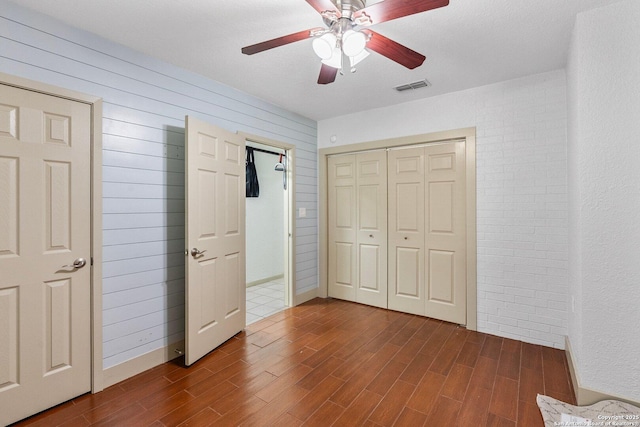 unfurnished bedroom featuring wooden walls, visible vents, ceiling fan, wood finished floors, and a closet