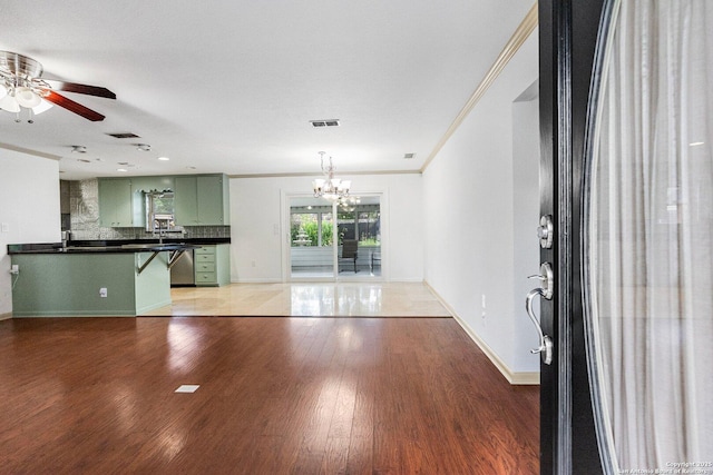 unfurnished living room with baseboards, visible vents, ornamental molding, wood finished floors, and ceiling fan with notable chandelier