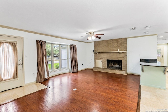 unfurnished living room featuring visible vents, a fireplace, ornamental molding, and wood finished floors