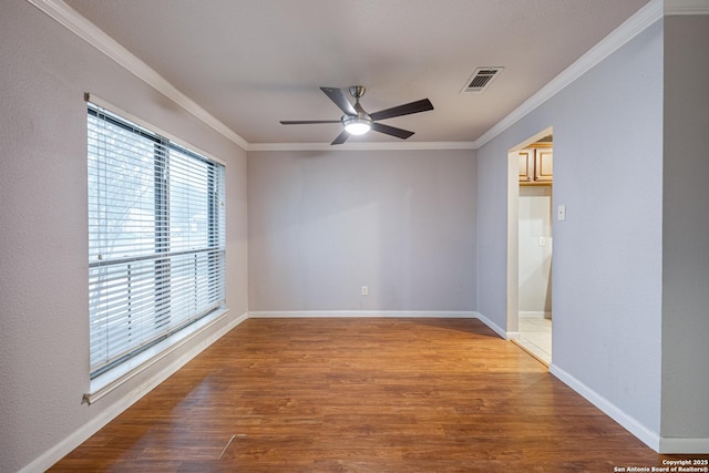 empty room featuring a ceiling fan, wood finished floors, baseboards, ornamental molding, and visible vents