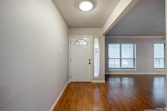 entryway with a textured wall, wood finished floors, baseboards, and ornamental molding