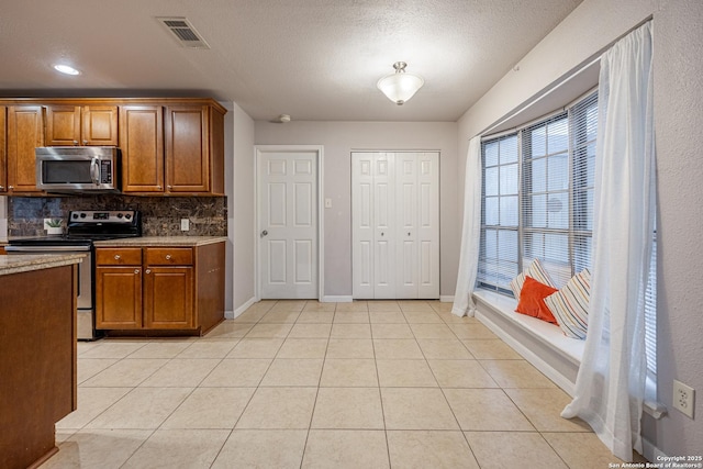 kitchen with brown cabinets, visible vents, light tile patterned floors, tasteful backsplash, and appliances with stainless steel finishes