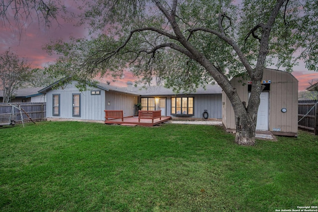 back of house at dusk featuring a lawn, a wooden deck, and a fenced backyard