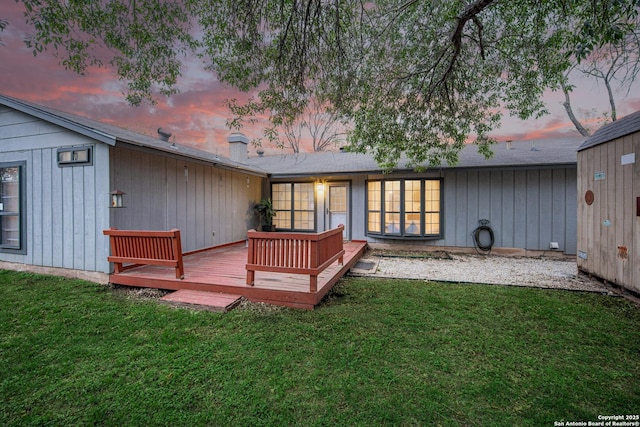 back of house at dusk with a wooden deck and a yard