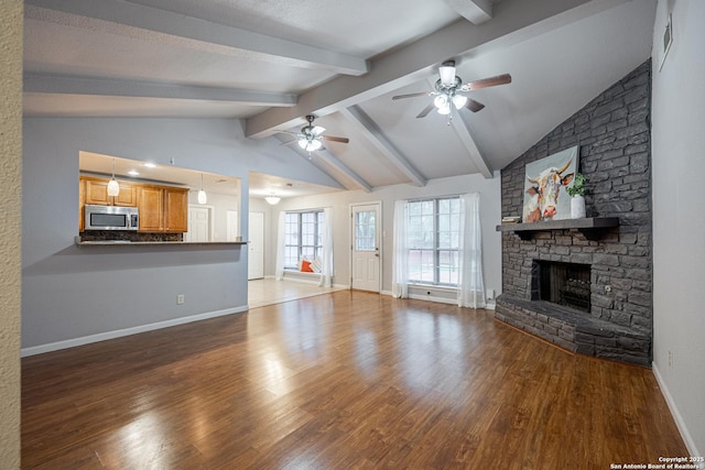unfurnished living room featuring lofted ceiling with beams, a stone fireplace, wood finished floors, and ceiling fan