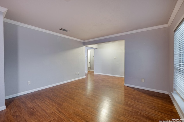 spare room with baseboards, wood finished floors, visible vents, and crown molding