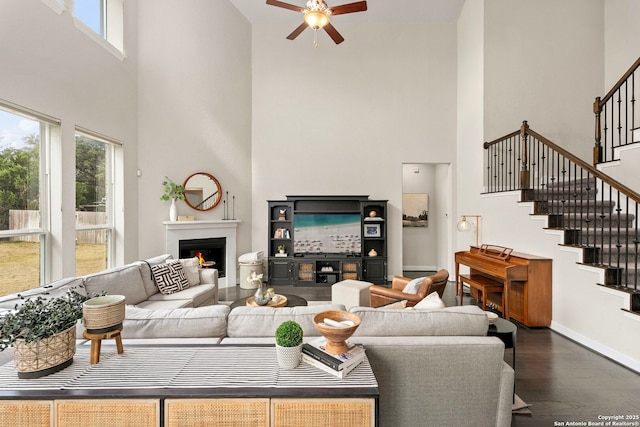 living room with a lit fireplace, stairway, plenty of natural light, and dark wood finished floors