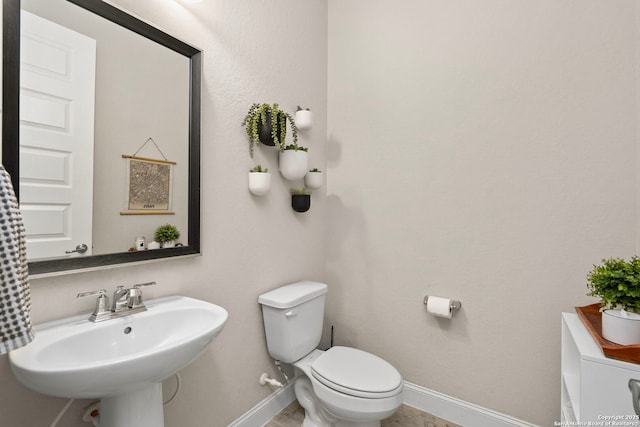 half bath featuring baseboards, a sink, and toilet