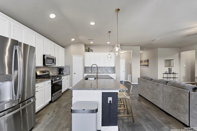 kitchen with a center island with sink, open floor plan, stainless steel appliances, white cabinetry, and a sink