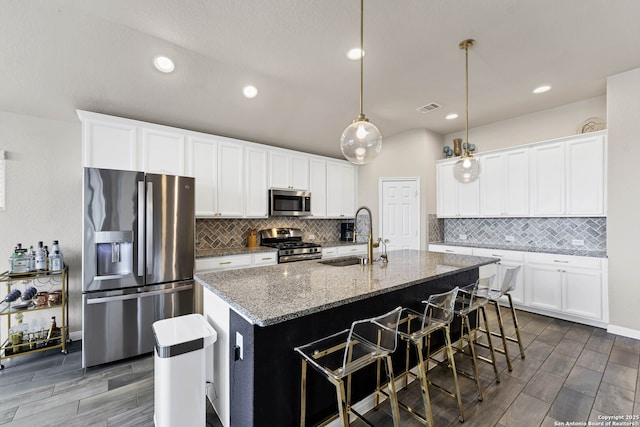 kitchen featuring stone counters, stainless steel appliances, a sink, visible vents, and an island with sink