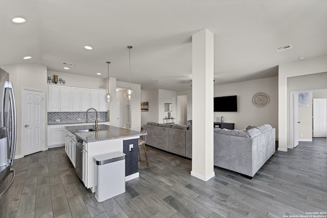 kitchen featuring a center island with sink, hanging light fixtures, decorative backsplash, open floor plan, and white cabinets