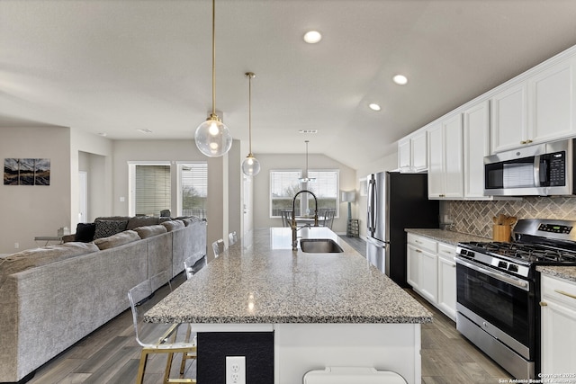 kitchen featuring stainless steel appliances, open floor plan, a kitchen island with sink, and decorative light fixtures