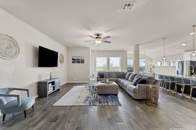 living area featuring visible vents, dark wood-type flooring, a ceiling fan, and baseboards