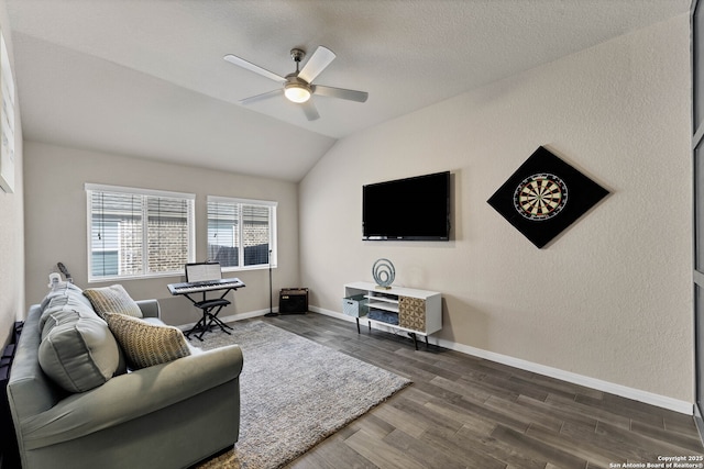 living area with lofted ceiling, ceiling fan, a textured wall, baseboards, and dark wood finished floors