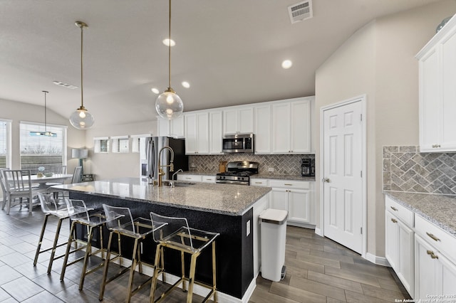 kitchen with a kitchen island with sink, stainless steel appliances, hanging light fixtures, light stone countertops, and a kitchen bar