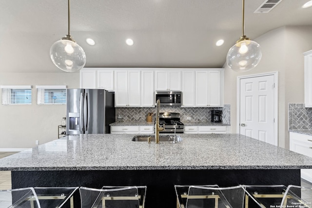 kitchen featuring appliances with stainless steel finishes, pendant lighting, a kitchen island with sink, and light stone counters