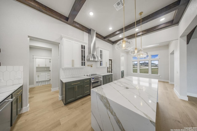 kitchen featuring glass insert cabinets, white cabinetry, wall chimney range hood, and light stone countertops