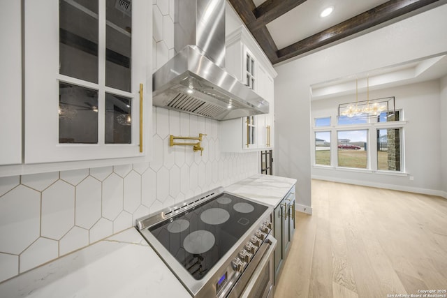 kitchen featuring glass insert cabinets, white cabinetry, wall chimney exhaust hood, and light stone countertops