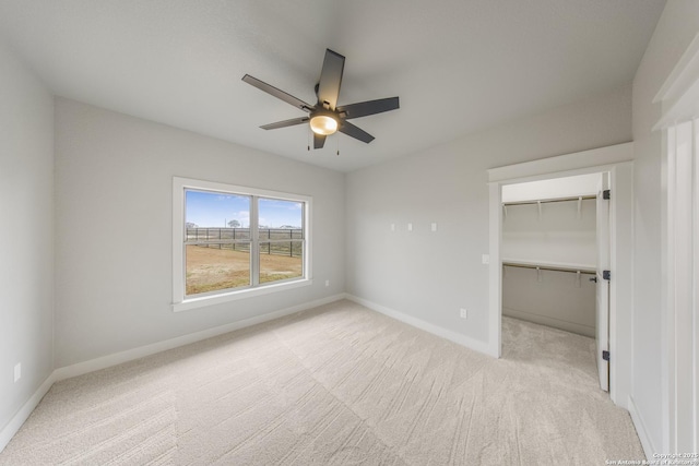 unfurnished bedroom with light carpet, ceiling fan, a walk in closet, and baseboards