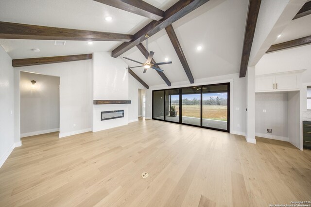 unfurnished living room with lofted ceiling with beams, a large fireplace, ceiling fan, light wood-type flooring, and baseboards