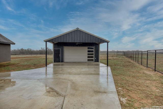 detached garage featuring a rural view, driveway, and fence