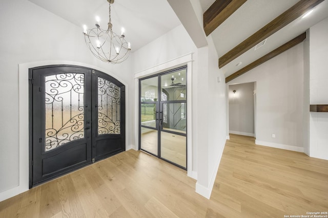 foyer entrance with lofted ceiling with beams, light wood-type flooring, a chandelier, and french doors