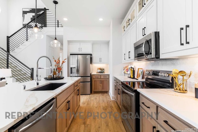 kitchen with glass insert cabinets, stainless steel appliances, white cabinetry, pendant lighting, and a sink