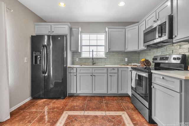 kitchen featuring appliances with stainless steel finishes, light countertops, a sink, and gray cabinetry