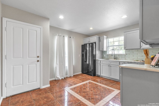 kitchen featuring a sink, black fridge with ice dispenser, light countertops, gray cabinets, and decorative backsplash