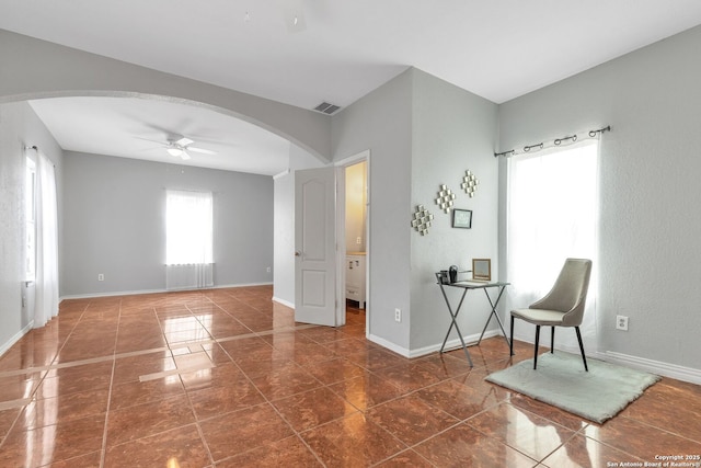 sitting room with baseboards, visible vents, arched walkways, a ceiling fan, and dark tile patterned floors