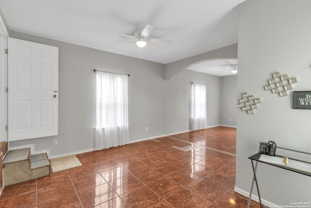 unfurnished living room with a ceiling fan, arched walkways, and baseboards