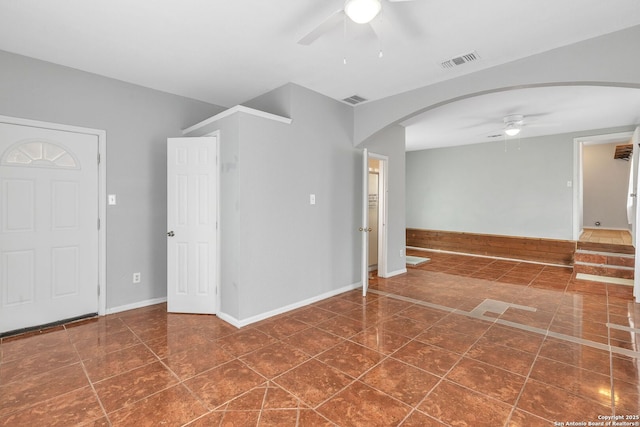 empty room with arched walkways, dark tile patterned floors, visible vents, baseboards, and a ceiling fan