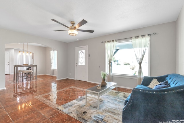 tiled entrance foyer featuring baseboards, arched walkways, and a ceiling fan