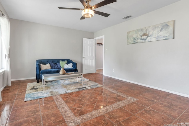 living area featuring a ceiling fan, dark tile patterned floors, visible vents, and baseboards