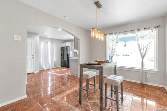 dining room featuring arched walkways, dark tile patterned floors, and baseboards