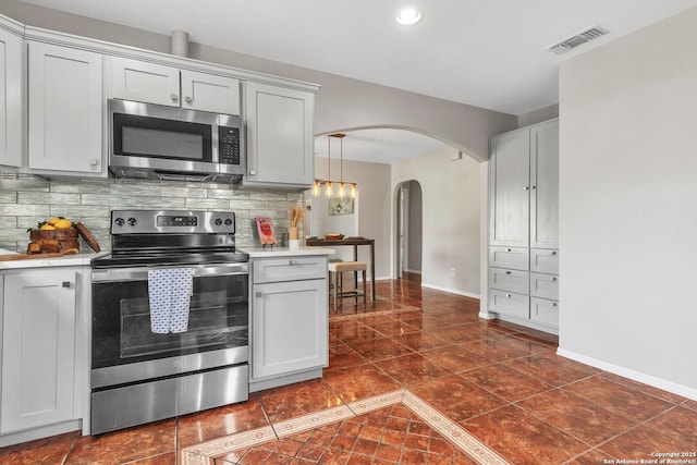 kitchen featuring arched walkways, tasteful backsplash, light countertops, visible vents, and appliances with stainless steel finishes