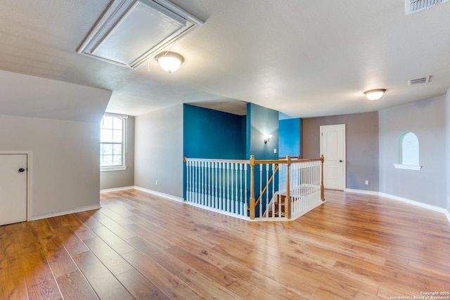 empty room with visible vents, wood finished floors, attic access, and baseboards